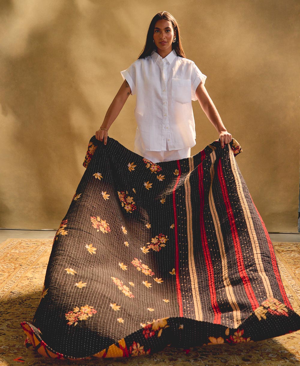 woman holding a black floral kantha quilt against a beige background