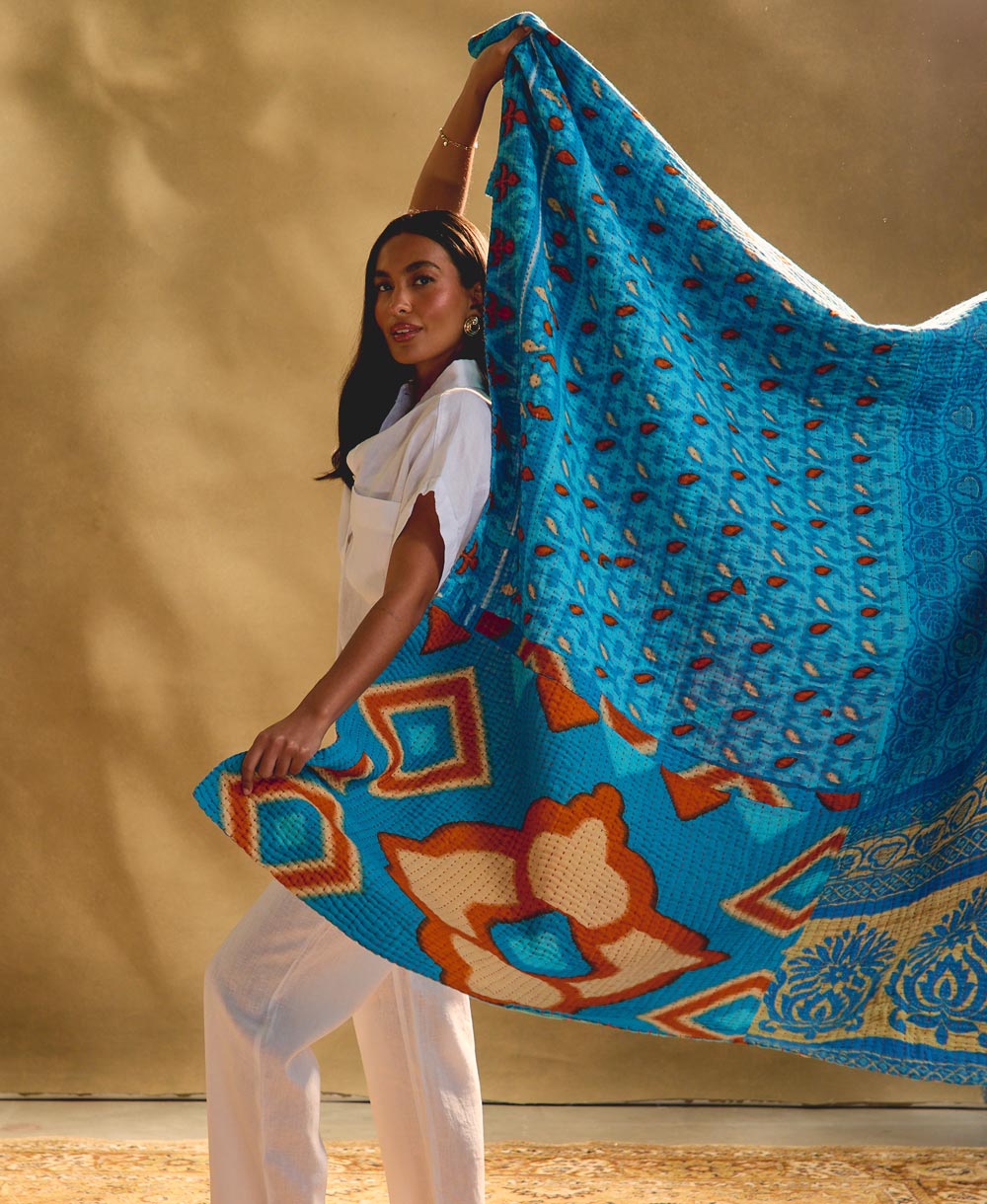 woman holding bright blue kantha quilt against a beige background