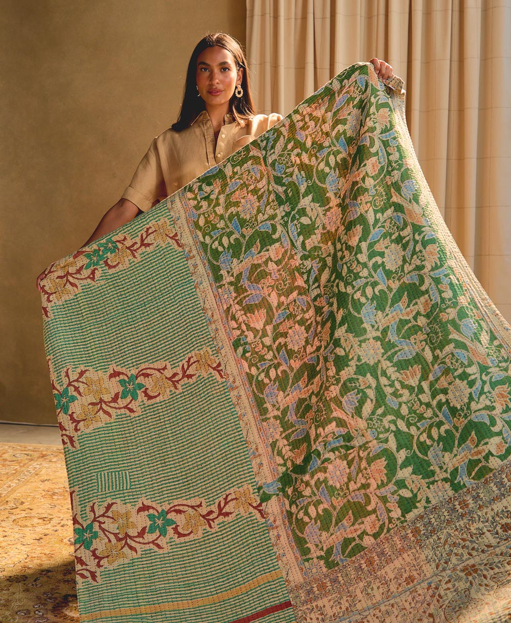 woman holding a green floral kantha quilt against a beige background