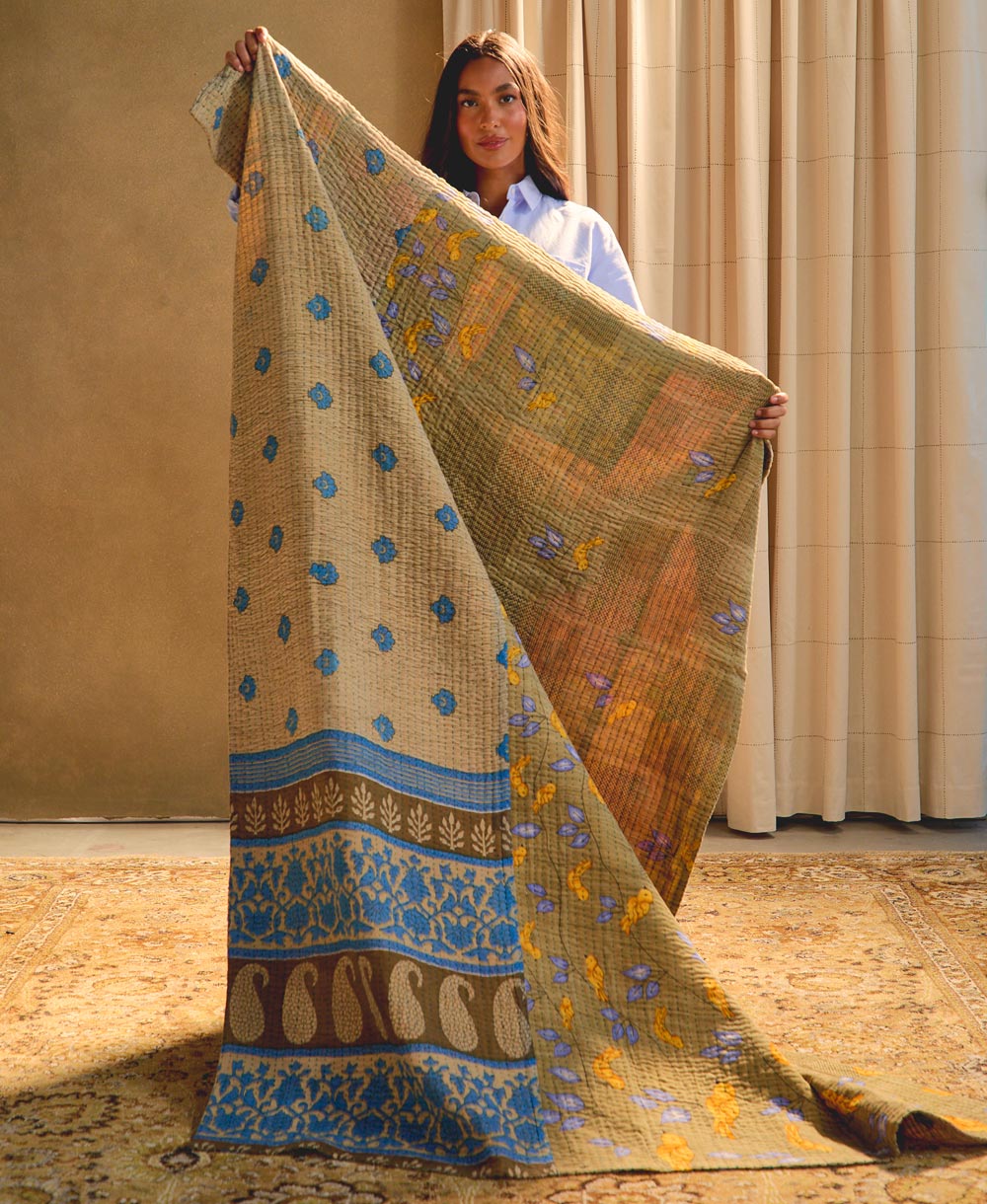 woman holding sage green kantha quilt against a beige background