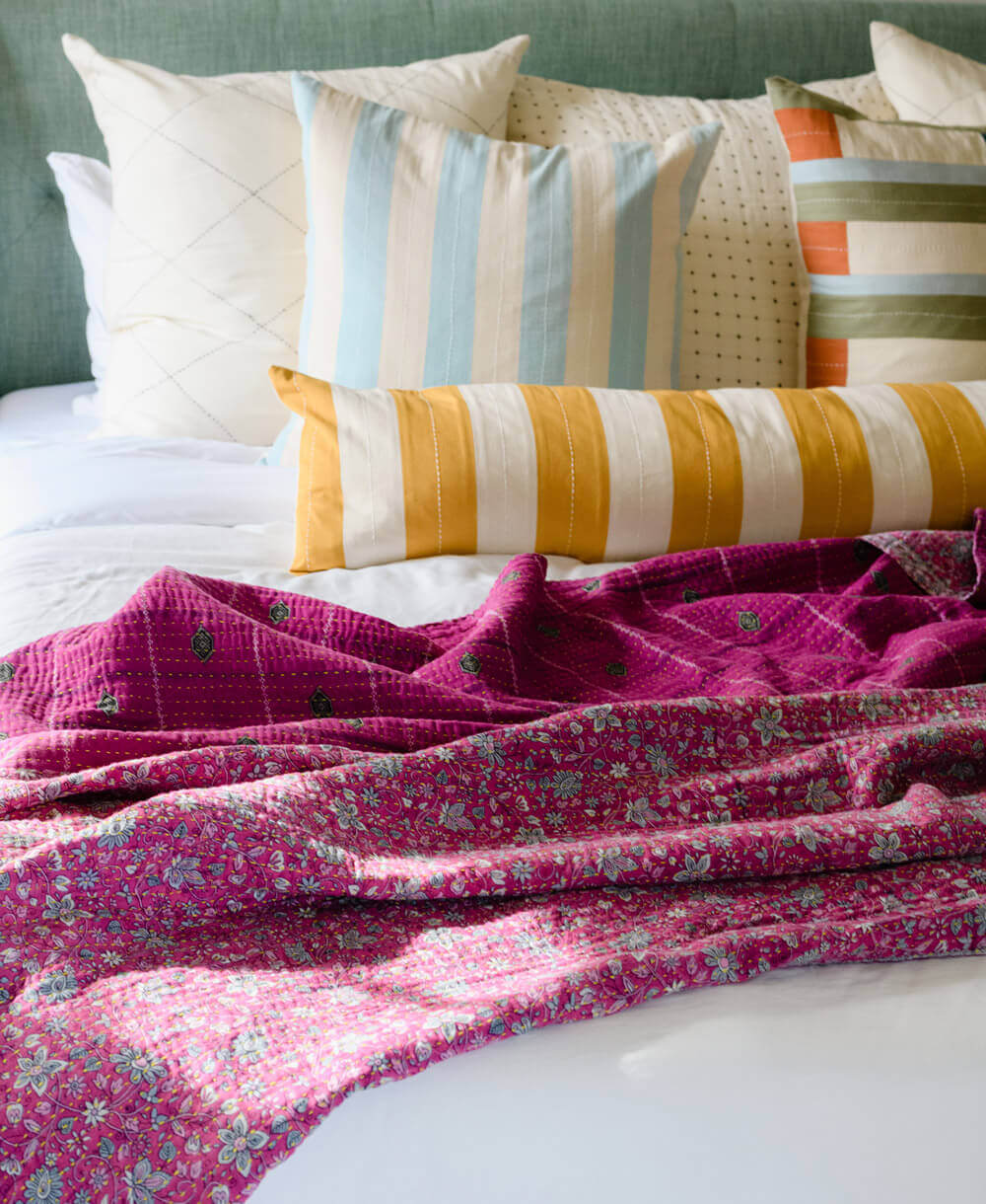 hot pink handmade kantha quilt draped on all white bed with colorful throw pillows