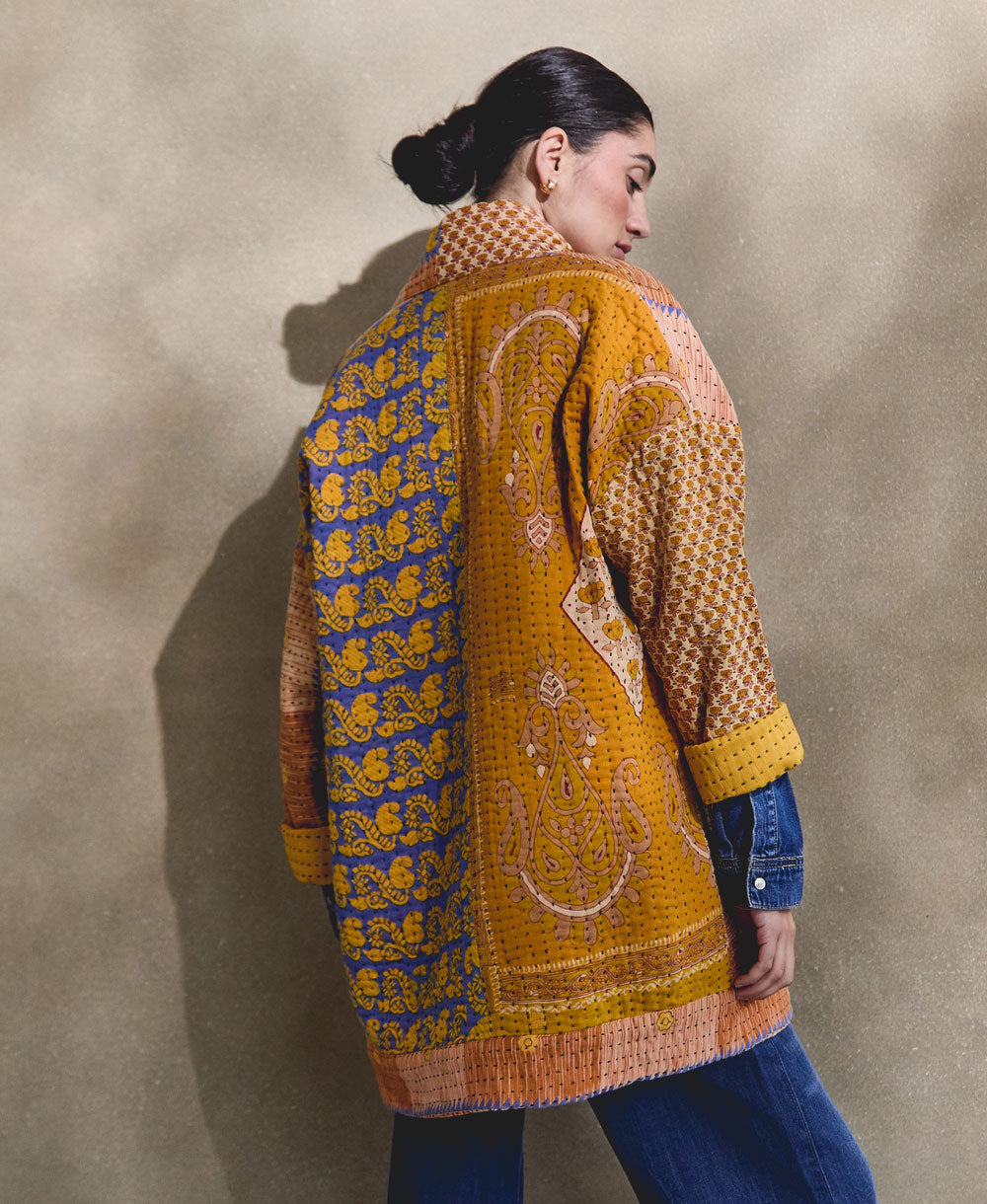 woman wearing mismatched back of kantha quilted jacket in shades of orange and blue