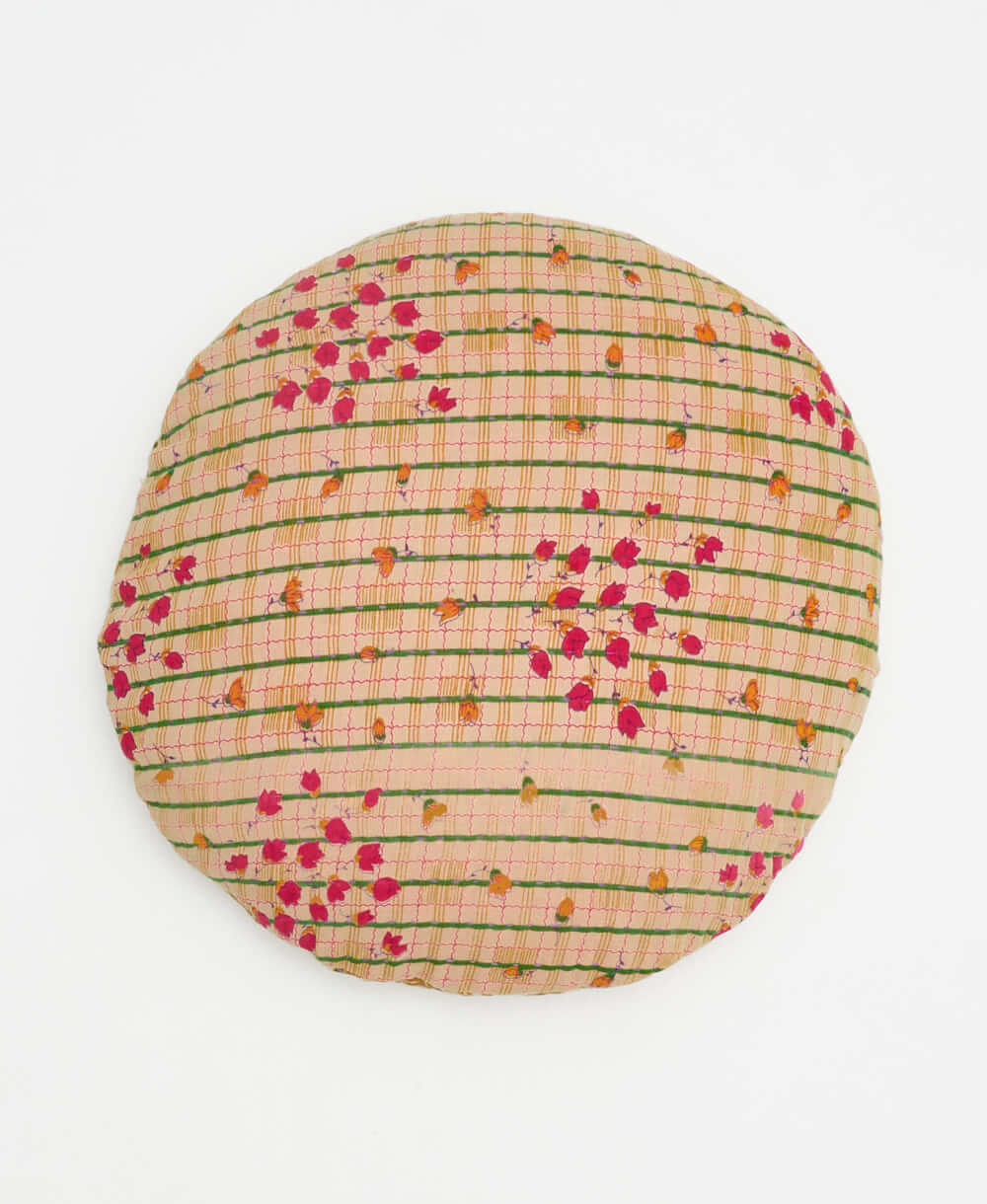 tan round pillow with a green and red grid and red and orange flowers 