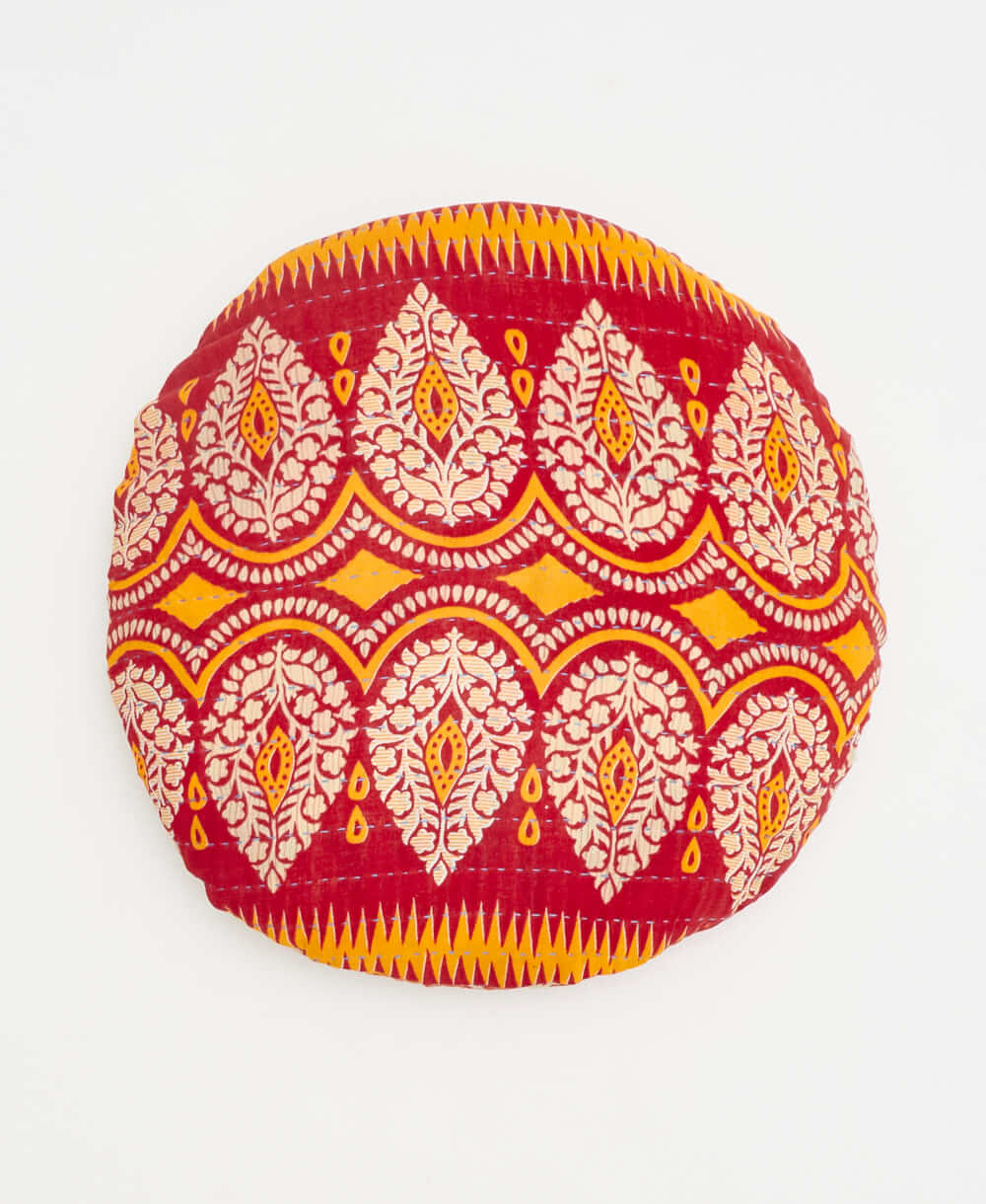 red round pillow with white and orange paisley details 