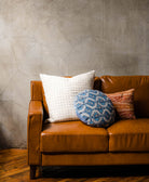 sustainable throw pillows on modern brown leather sofa in blue, orange and white made from sustainable materials