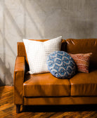 blue round pillow, white square pillow and orange paisley pillow on brown leather couch by Anchal