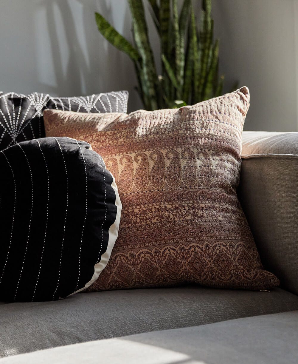 lavender throw pillow in paisley print with hand-stitched embroidery made in India sitting on light grey sofa