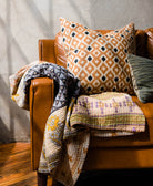 modern boho square pillow in brown & black ikat print sitting on modern brown camel sofa