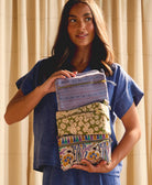 Woman holding a stack of colorful cosmetic bags against a beige curtain background