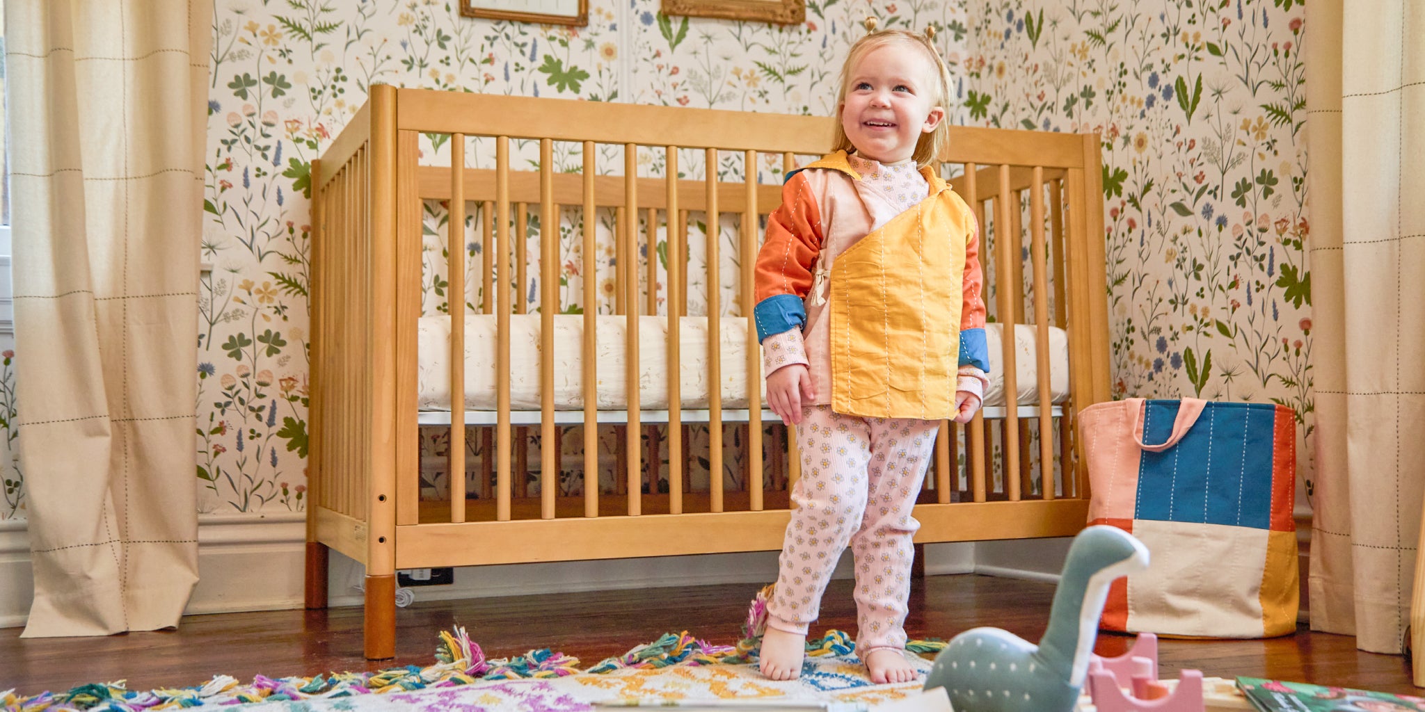 toddler wearing colorful rainbow hoodie with wrap front in bedroom with floral wallpaper