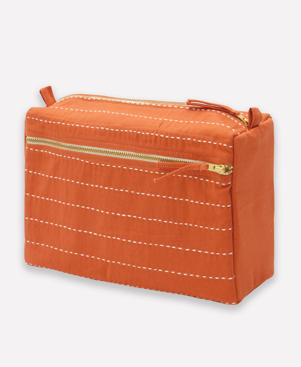 Orange toiletry bag with white stitching on a light gray background