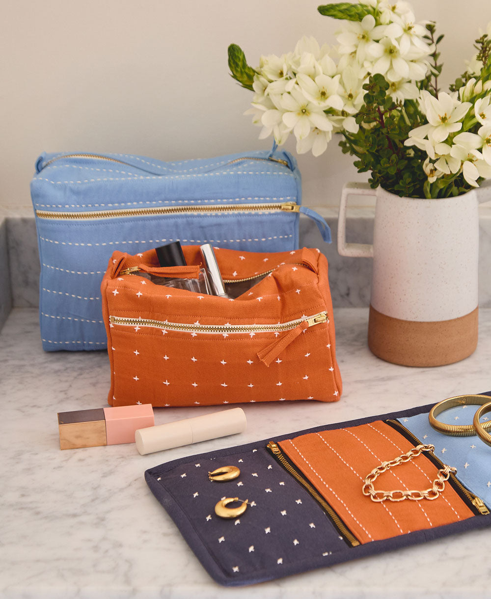 large blue toiletry bag and orange toiletry bag sitting on gray bathroom countertop with matching orange and blue travel organizer