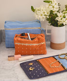 large blue toiletry bag and orange toiletry bag sitting on gray bathroom countertop with matching orange and blue travel organizer