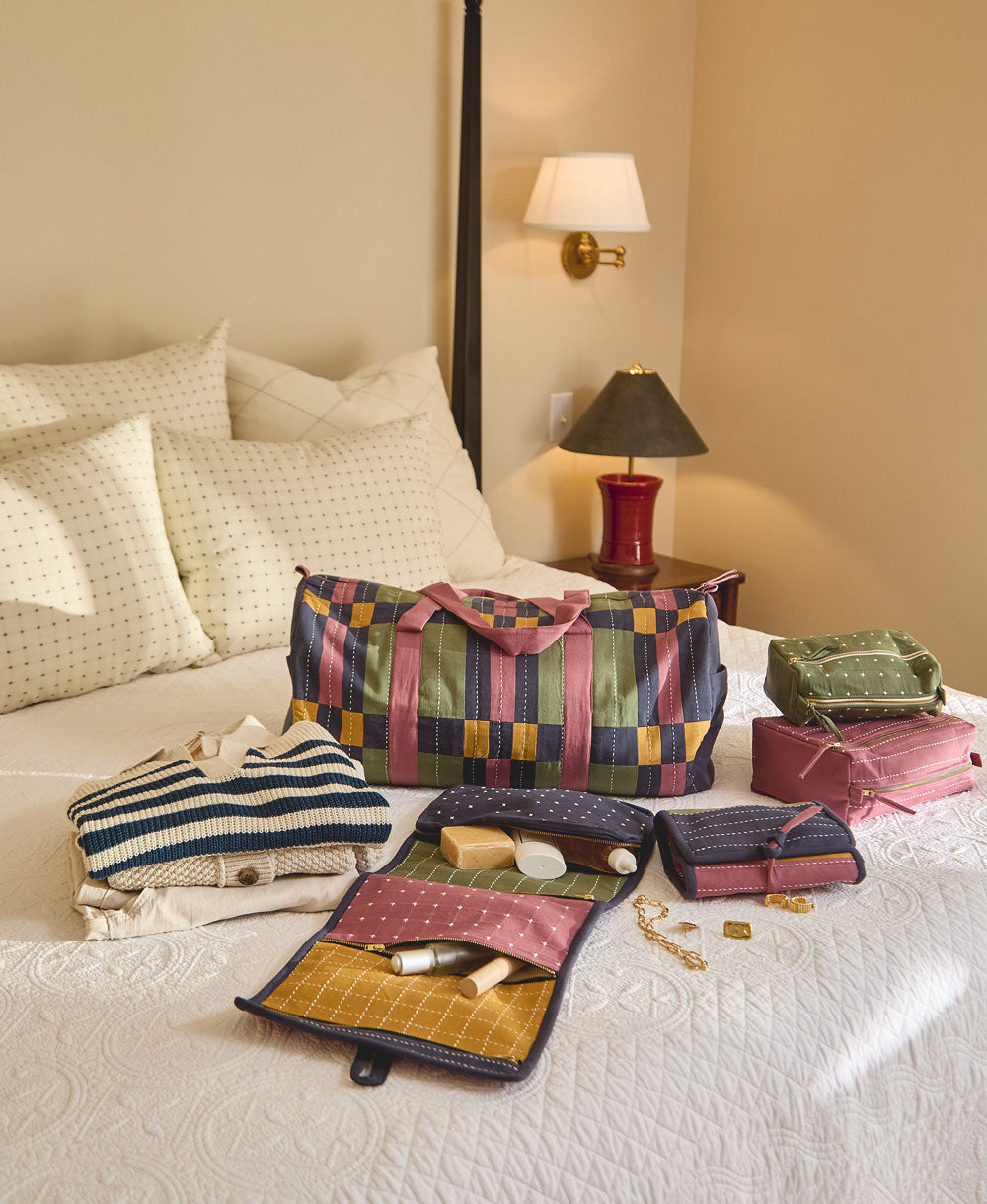 checkered duffle bag on white bedspread with other toiletry bags in coordinating colors