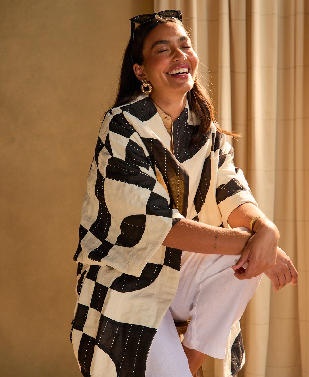 woman laughing while wearing black and white marquise cocoon quilted jacket in front of a beige background