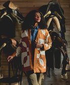 woman wearing white and camel quilted jacket amongst saddles in horse barn setting
