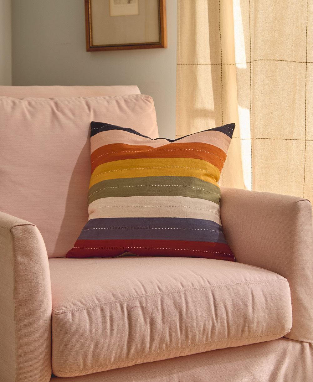 Colorful striped pillow on a pink armchair with a neutral background