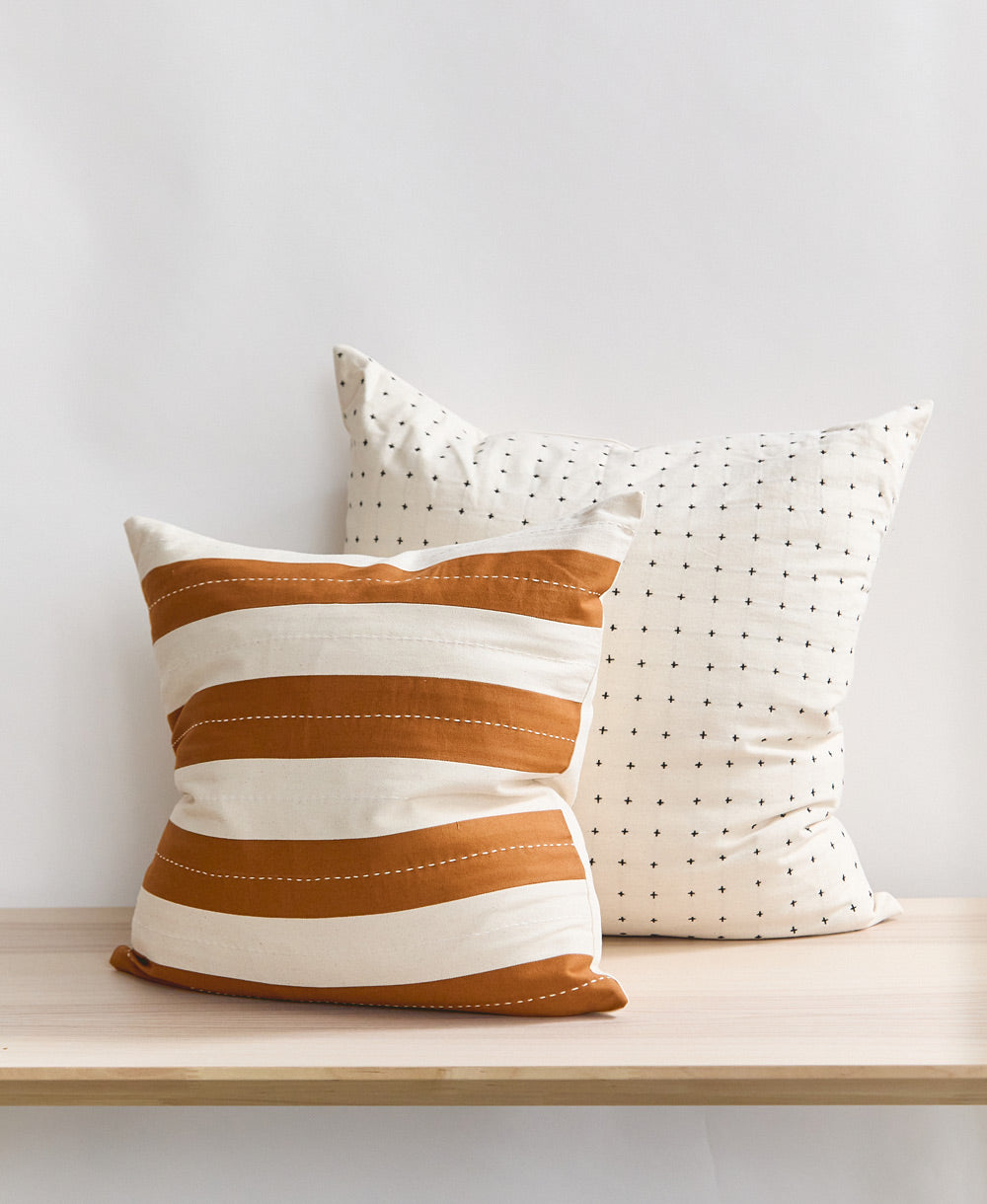 striped throw pillow with white cross-stitch pillow sitting on natural wooden bench