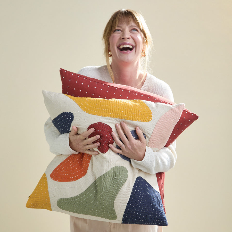 woman holding two throw pillows with geometric petal shapes and embroidery on them