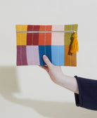 Colorful patchwork pouch with a tassel held by a hand against a white background