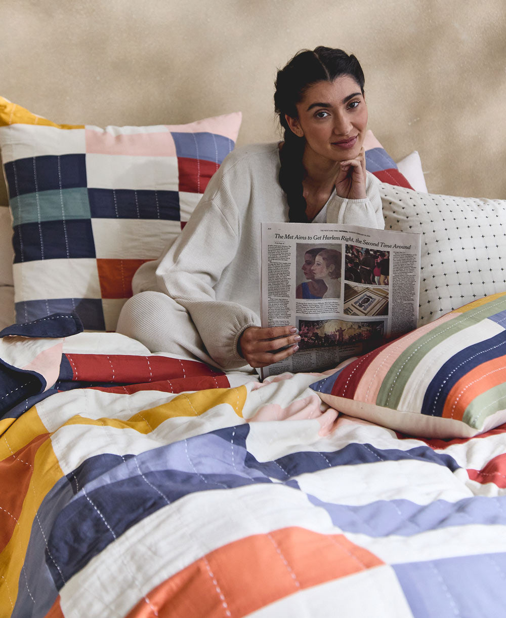 woman reading newspaper in colorful checkered bedding handmade in India in a rainbow of colors