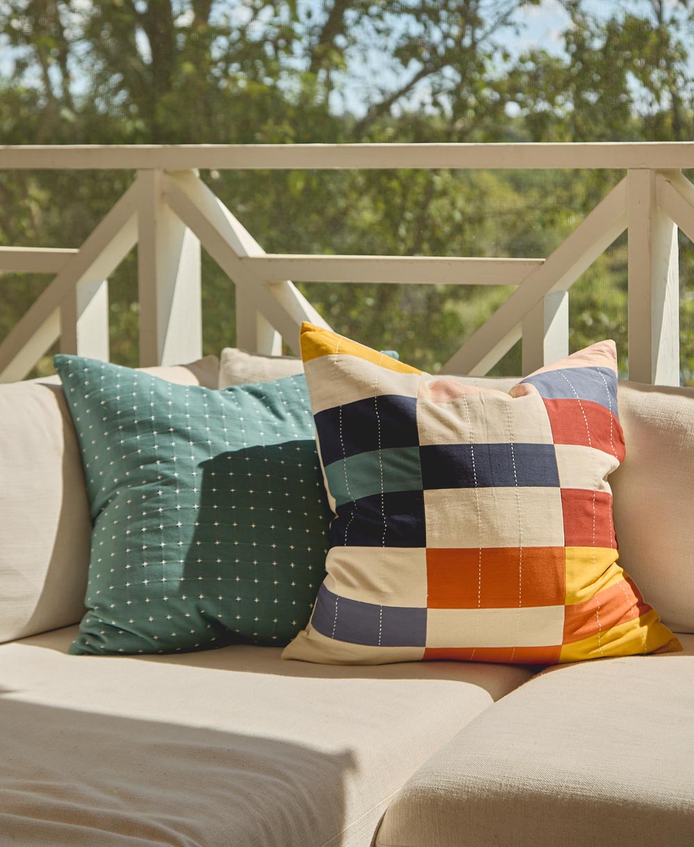 Colorful patchwork pillow on a beige sofa with a blurred green outdoor background