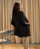 the back of woman standing against chair in quilted black cocoon jacket