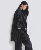 woman wearing naari cocoon quilted jacket in black with white embroidery carrying black braided sandals