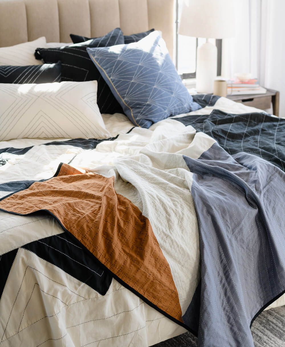 modern patchwork quilt in black, blue and camel draped over black and white comforter