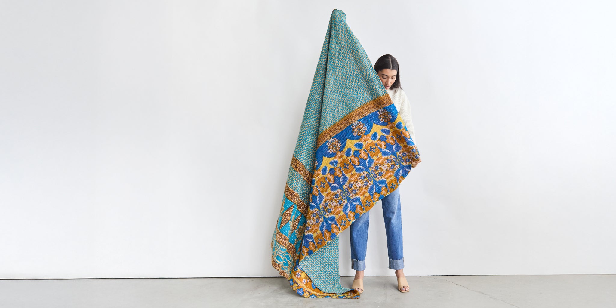 woman holding open vintage blue kantha quilt with orange floral print handmade in India by women artisans