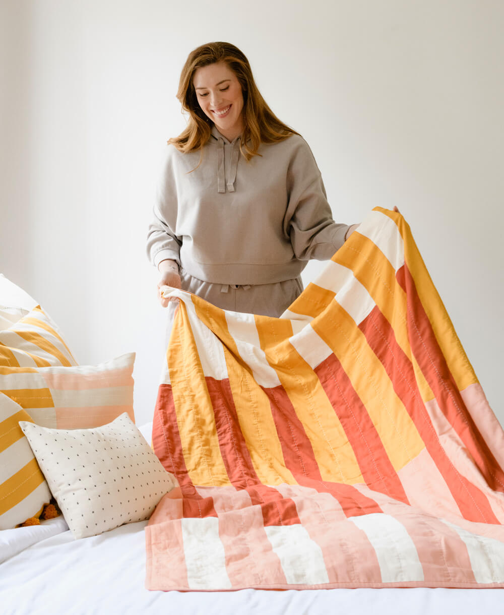 woman putting mustard, pink and orange offset patchwork quilt on bed