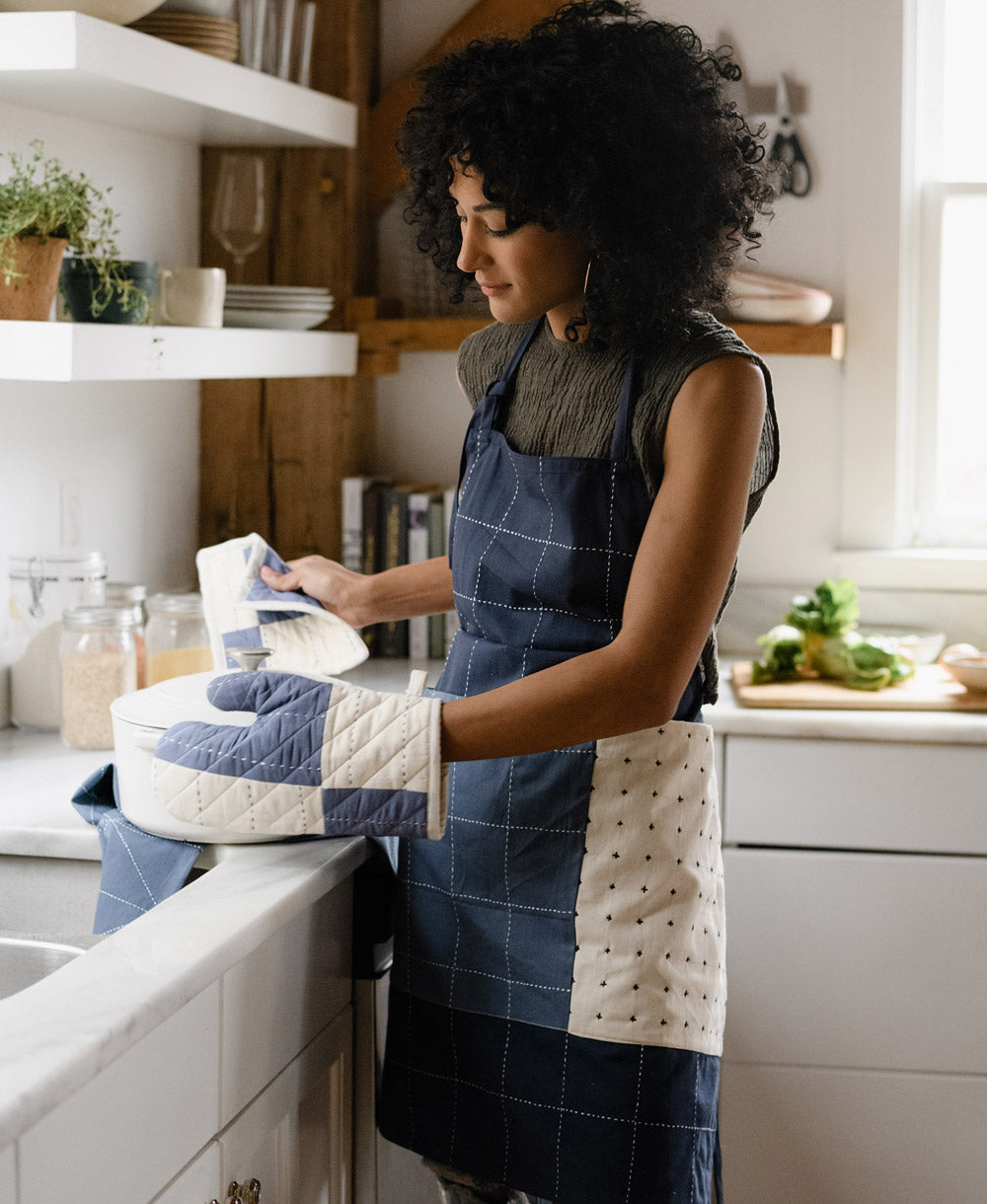 woman wearing navy blue colorblock bib apron in modern white kitchen with matching oven mitt