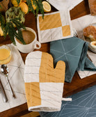 mustard yellow and natural white oven mitt on wooden table with matching pot holder