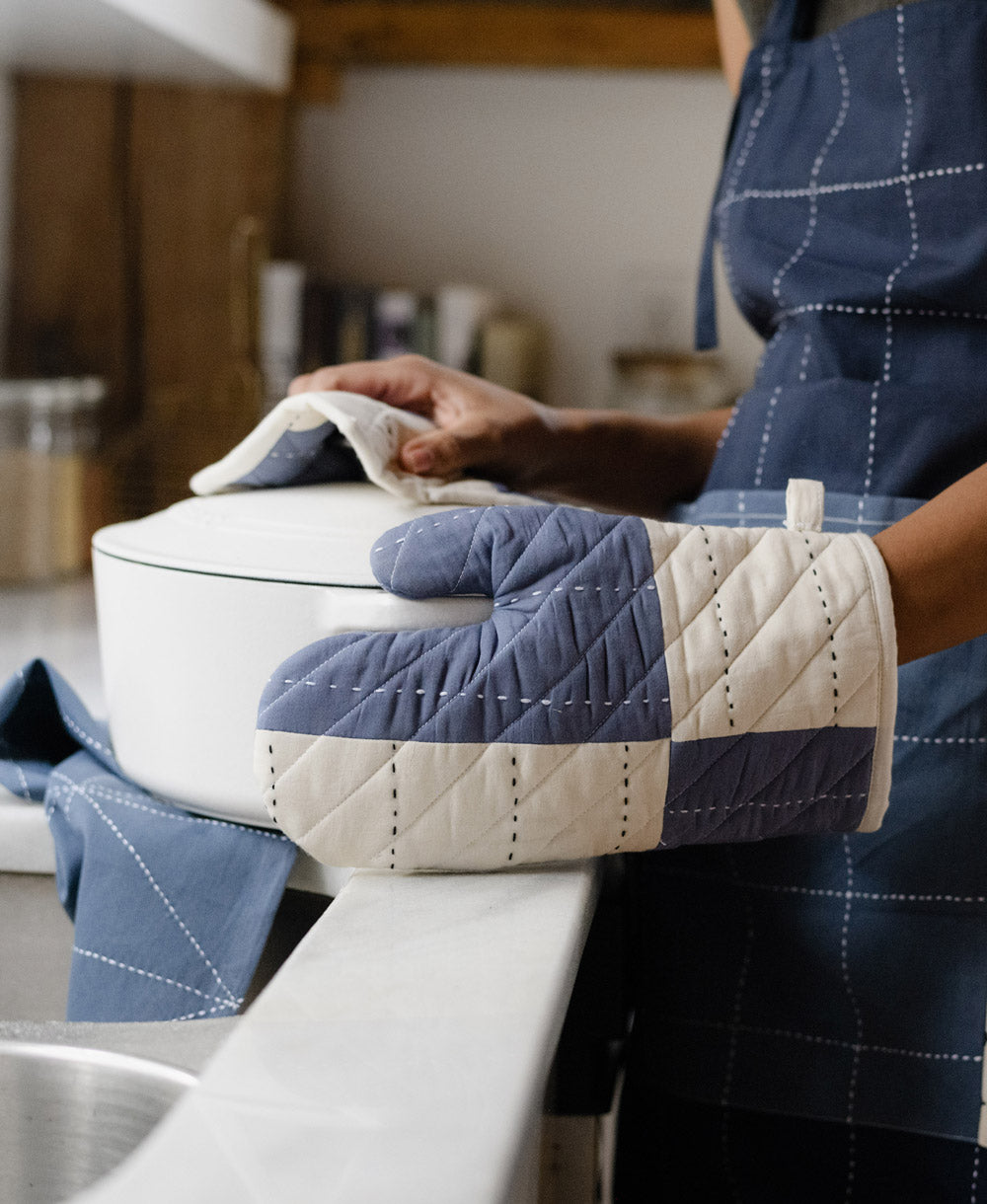 person wearing slate blue and white quilted oven mitt with coordinating organic cotton navy blue apron by Anchal