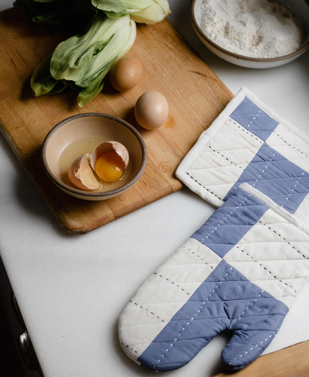 slate blue oven mitt and matching pot holder next to light wooden cutting board