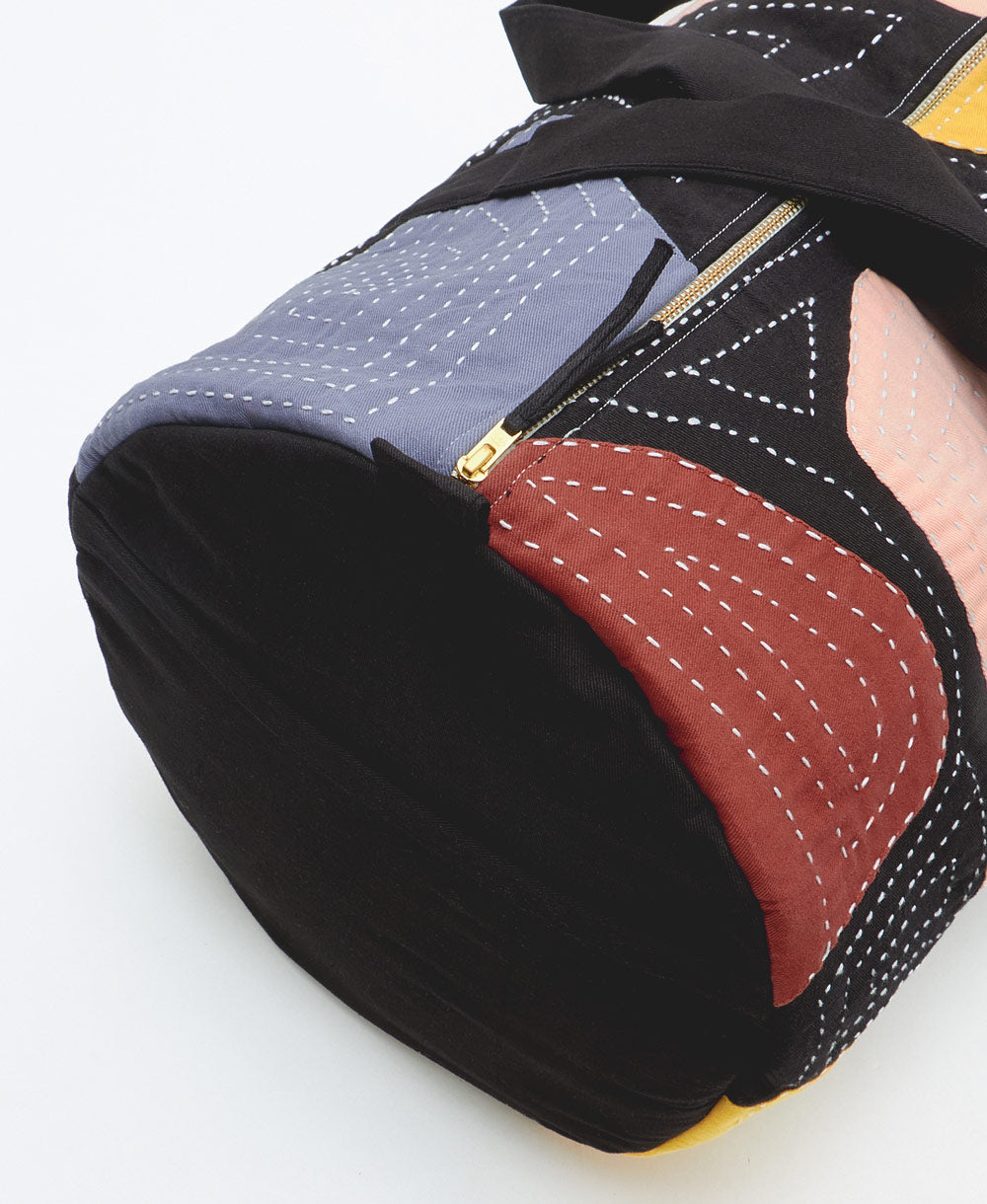 black canvas duffle bag with gold-tone zipper and exterior slip pockets with colorful patchwork