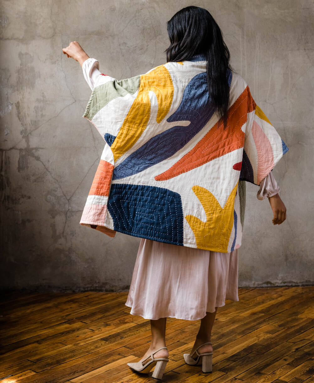 woman wearing quilted floral jacket in white with colorful petal-shaped applique details in cocoon silhouette