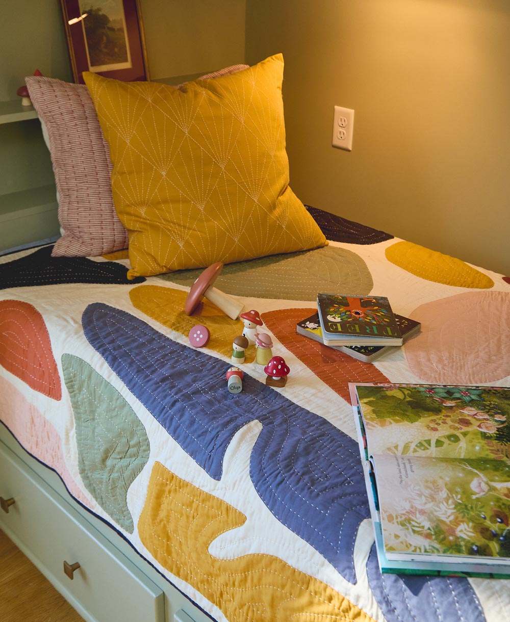 Colorful quilt with animal patterns on a bed, featuring books and toys