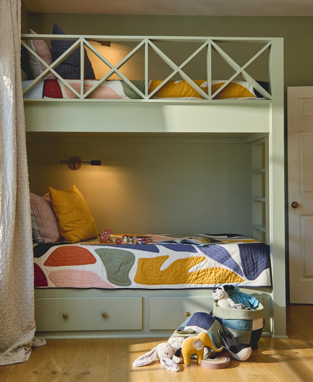 Children's bedroom with a green bunk bed featuring colorful bedding and toys on a wooden floor