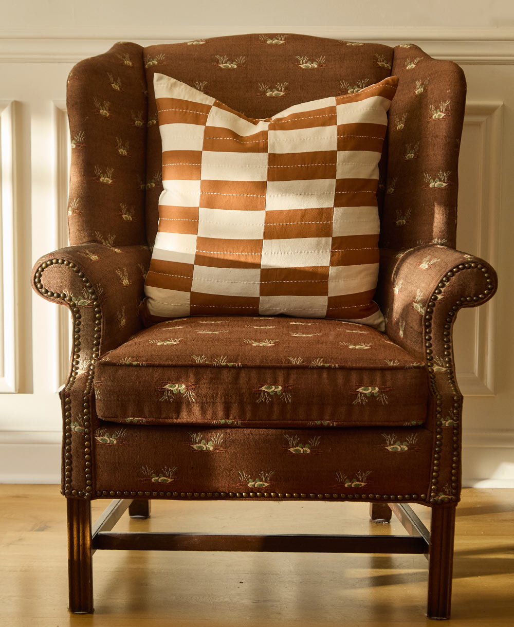 camel brown and white checkered pillow sitting on a vintage style brown upholstered chair
