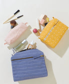 Blue pouch with white stripes, yellow pouch with white polka dots, makeup items on a light background