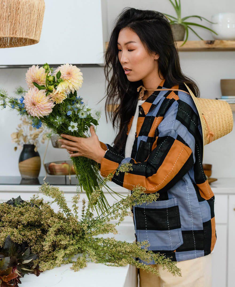 woman making a bouquet wearing blue, black & camel chore jacket with button closure