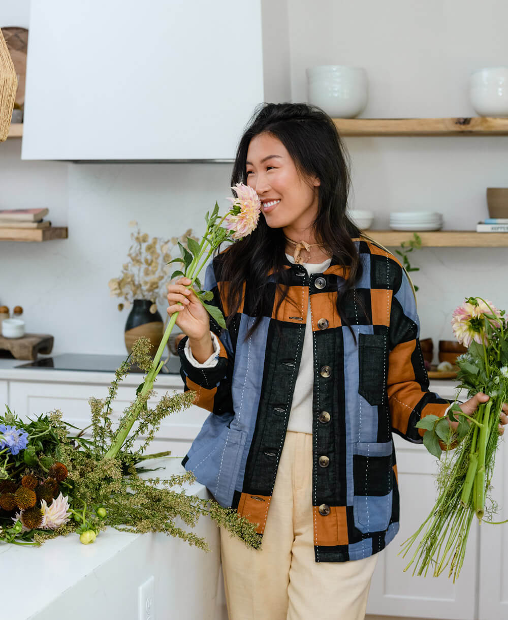 woman smelling fresh flowers wearing organic cotton plaid chore jacket with embroidery