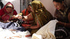 group of Anchal artisans sewing various organic cotton quilts outdoors using kantha stitching techniques