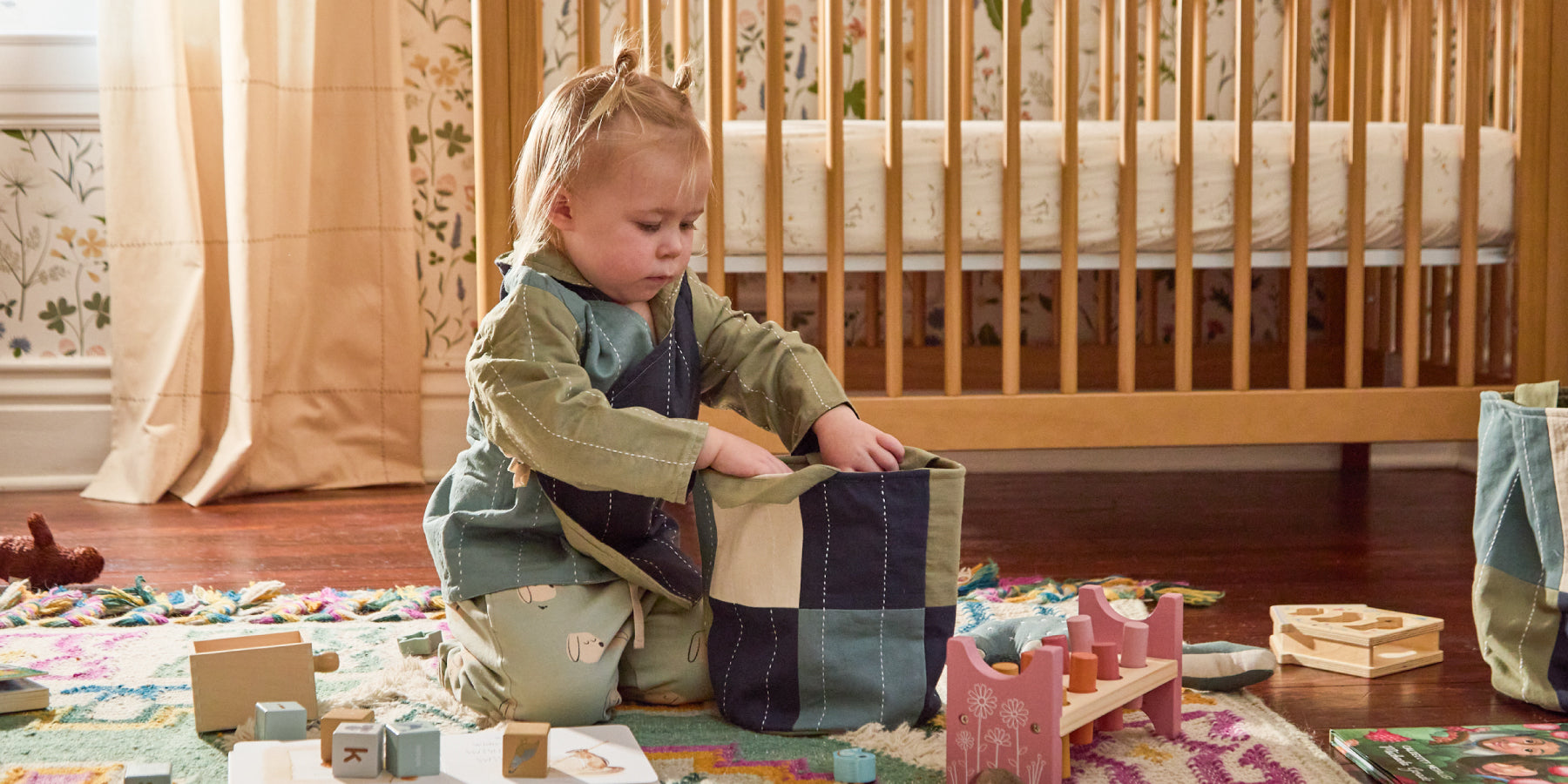 toddler wearing blue, green and navy colorblock wrap style hoodie putting blocks into matching fabric basket