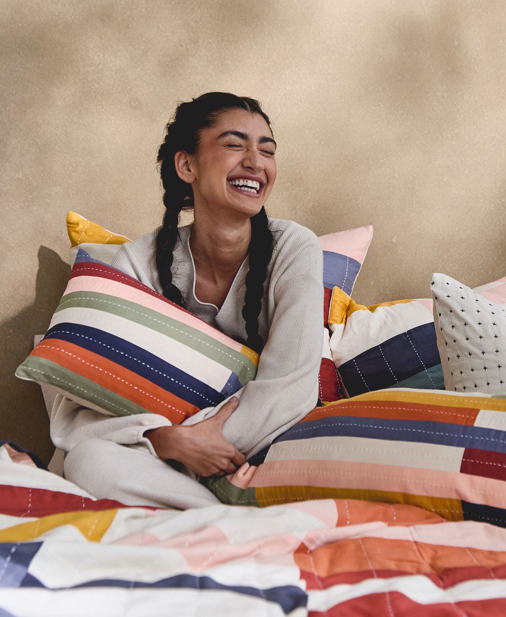 woman sitting on bed hugging decorative striped long lumbar pillow