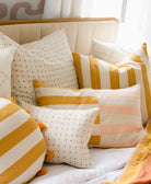 Decorative pillows with yellow and white stripes on an all white bed with a cream velvet and gold headboard