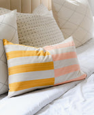 colorful pink and yellow striped lumbar pillow on all white bed