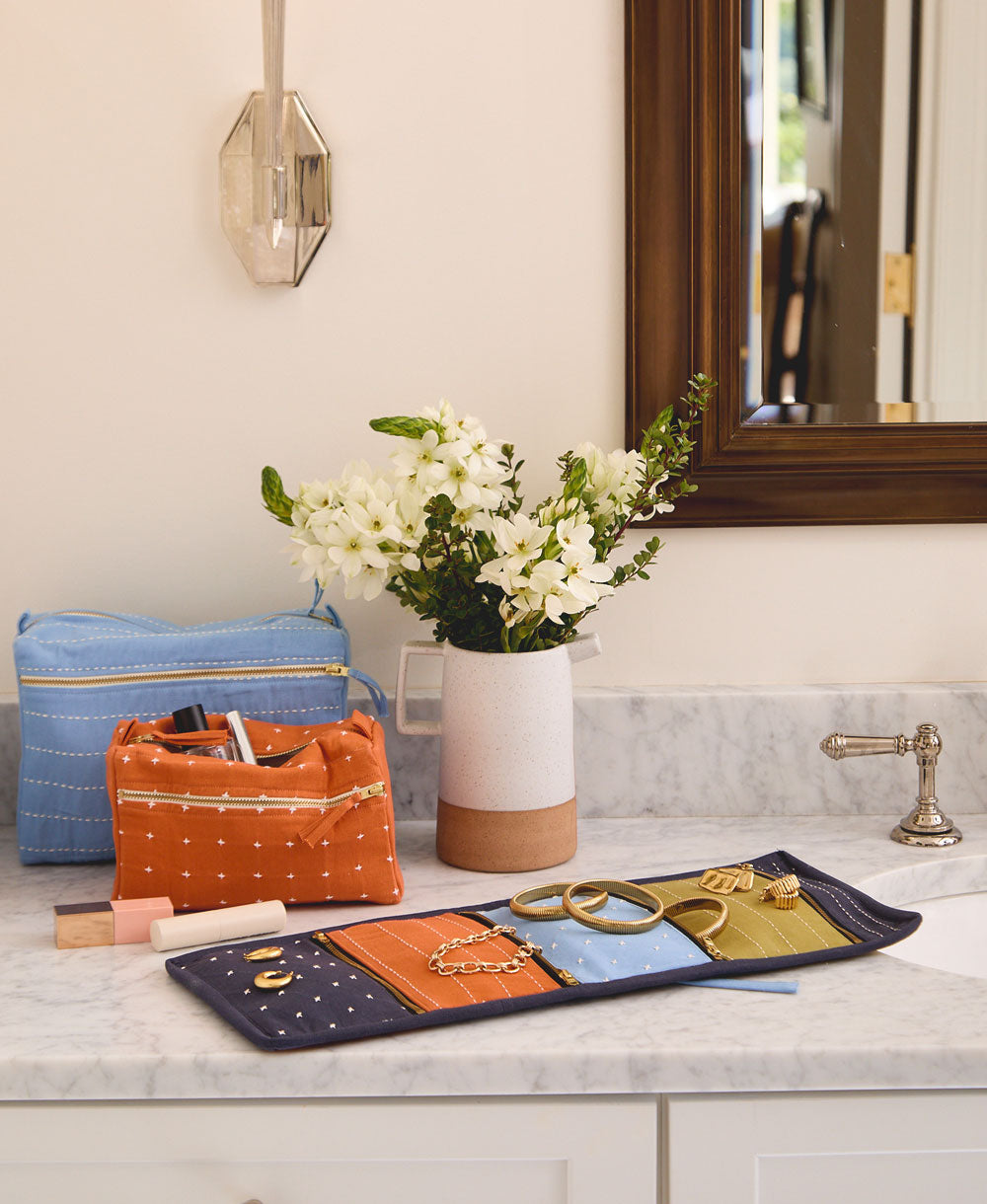 travel organizer for jewelry sitting on gray bathroom vanity with other colorful toiletry bags