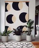 light wooden quilt hanger holding Anchal's crescent lattice quilt against white wall with potted houseplants in modern pots